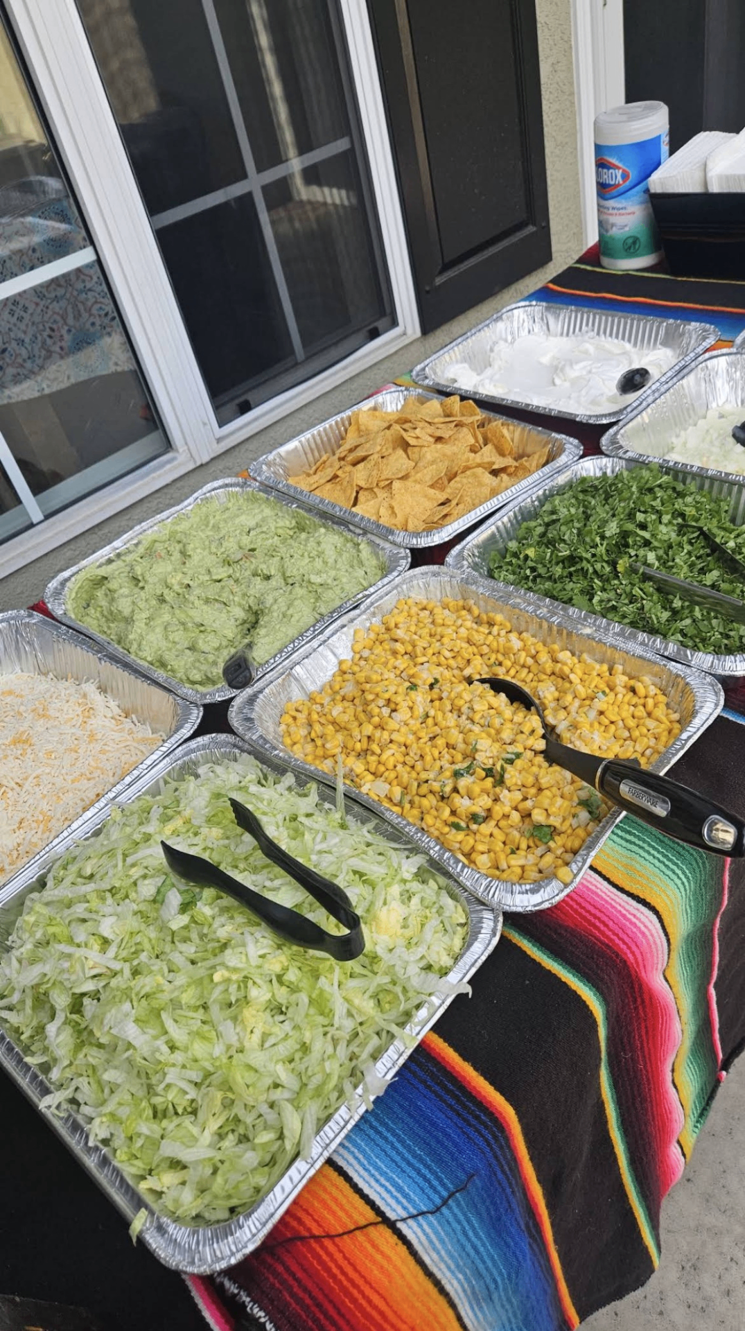 Catered toppings bar with guacamole, shredded lettuce, corn, cilantro, onions, cheese, sour cream and tortilla chips in serving trays