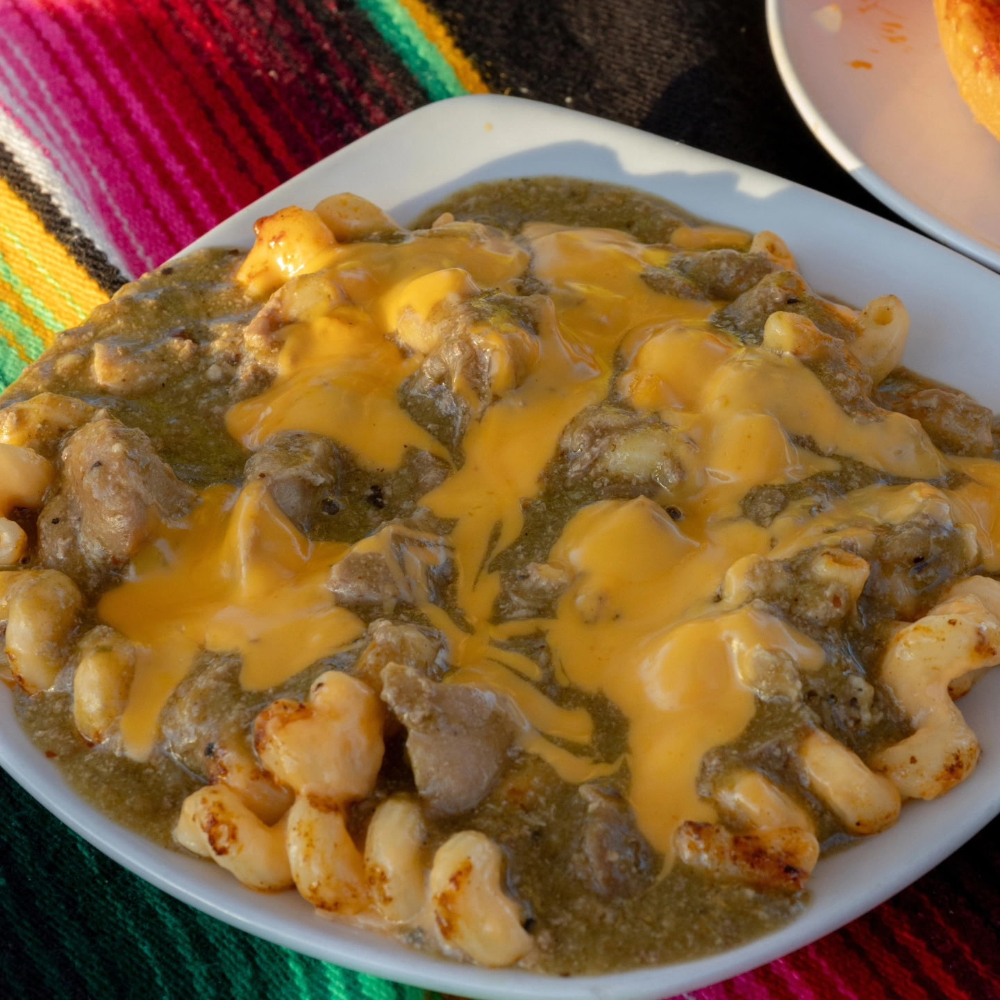Close-up of mac and cheese chili verde topped with melted cheddar and slow-cooked pork