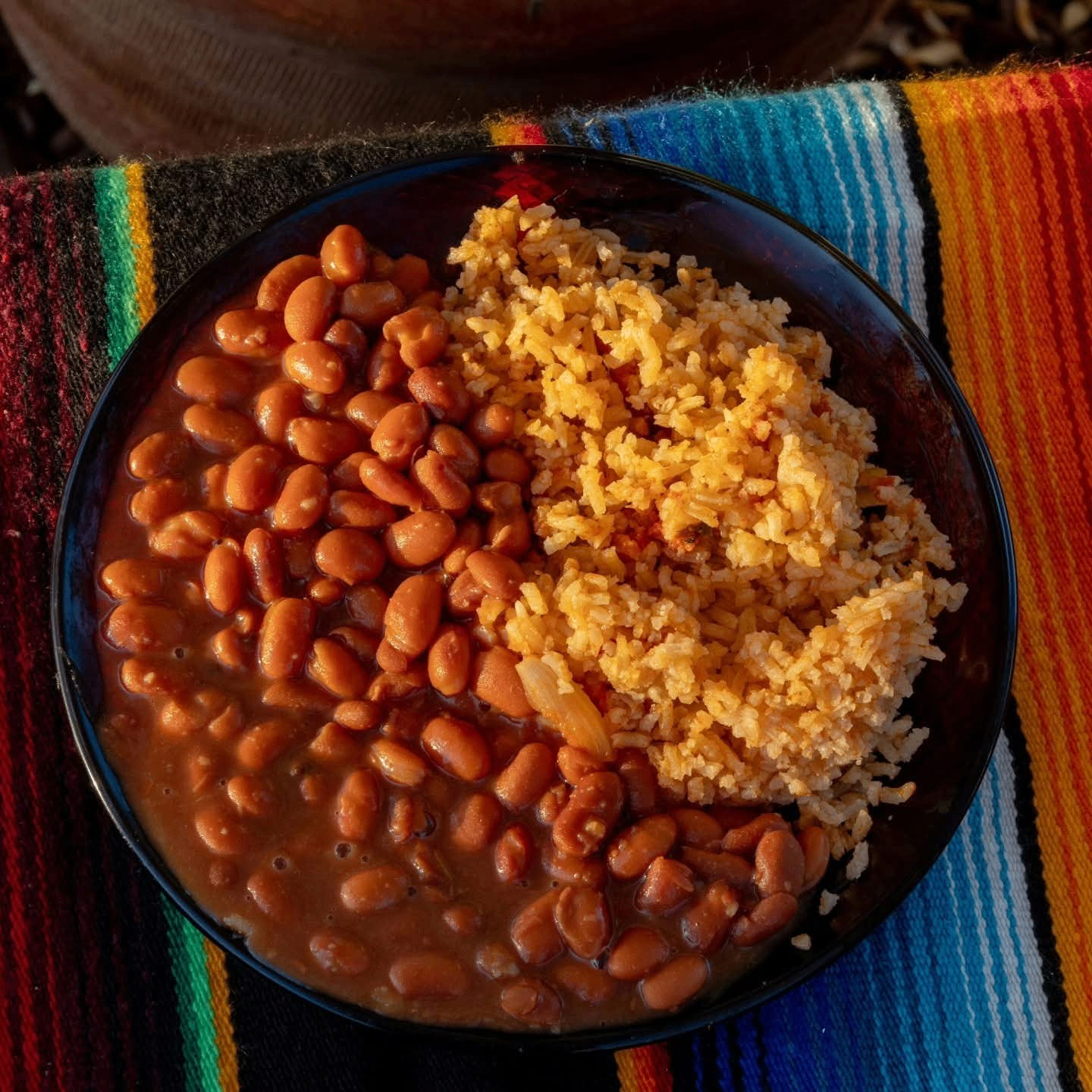 Black bowl of Mexican rice and whole pinto beans on a colorful striped tablecloth